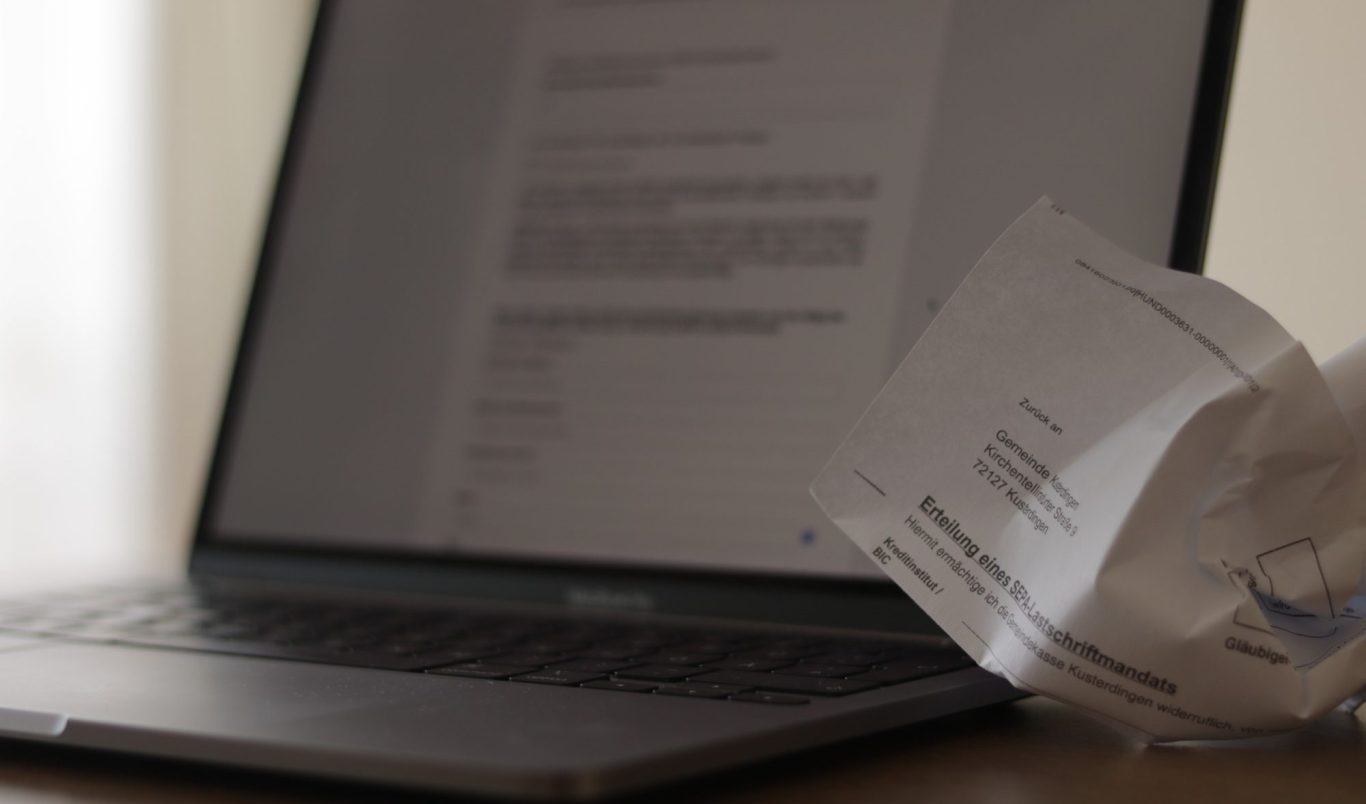 Digitales Rathaus: Mehr Service, weniger Wartezeit Ein Laptop zeigt eine moderne Benutzeroberfläche für digitale Verwaltungsdienstleistungen. Daneben ein Papierformular der Gemeinde.